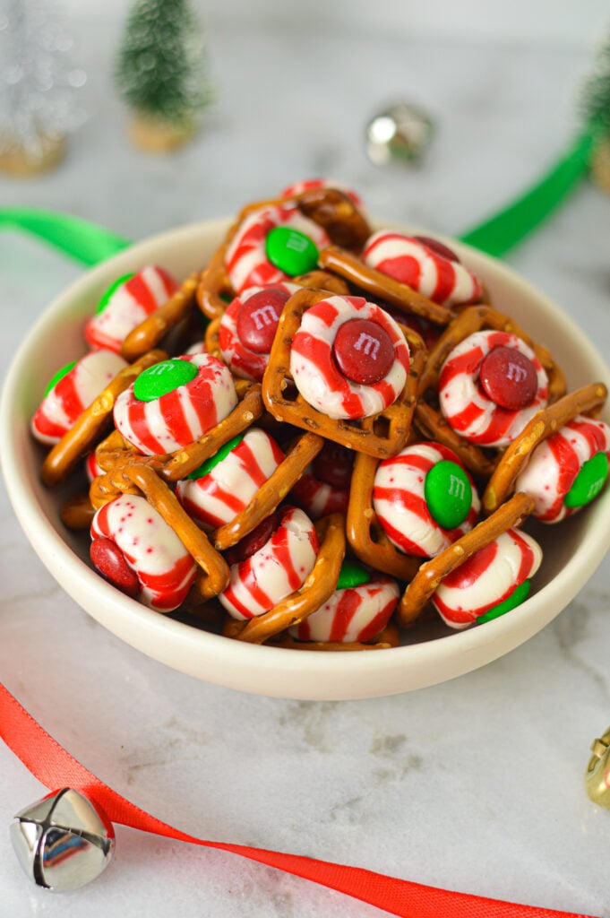 A small bowl full of Peppermint Kiss Pretzels, with the red and green m&ms atop the half melted Hershey's Peppermint kisses.