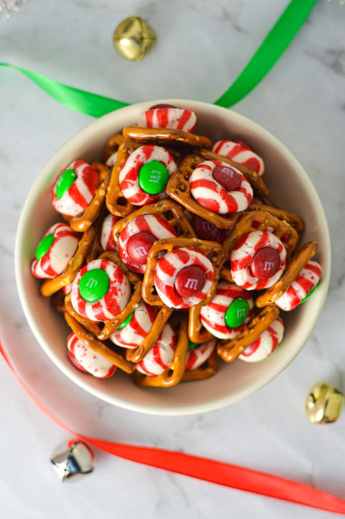 A shallow bowl full of Peppermint Kiss Pretzels, with some green and red ribbons and bells in the background, giving it a Christmas feel.
