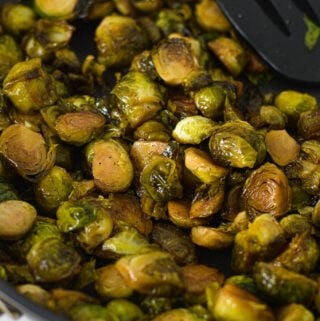 Some lightly browned Stovetop Balsamic Honey Brussels Sprouts in a large skillet, with a large spatula resting on top of the cooked brussels sprouts.