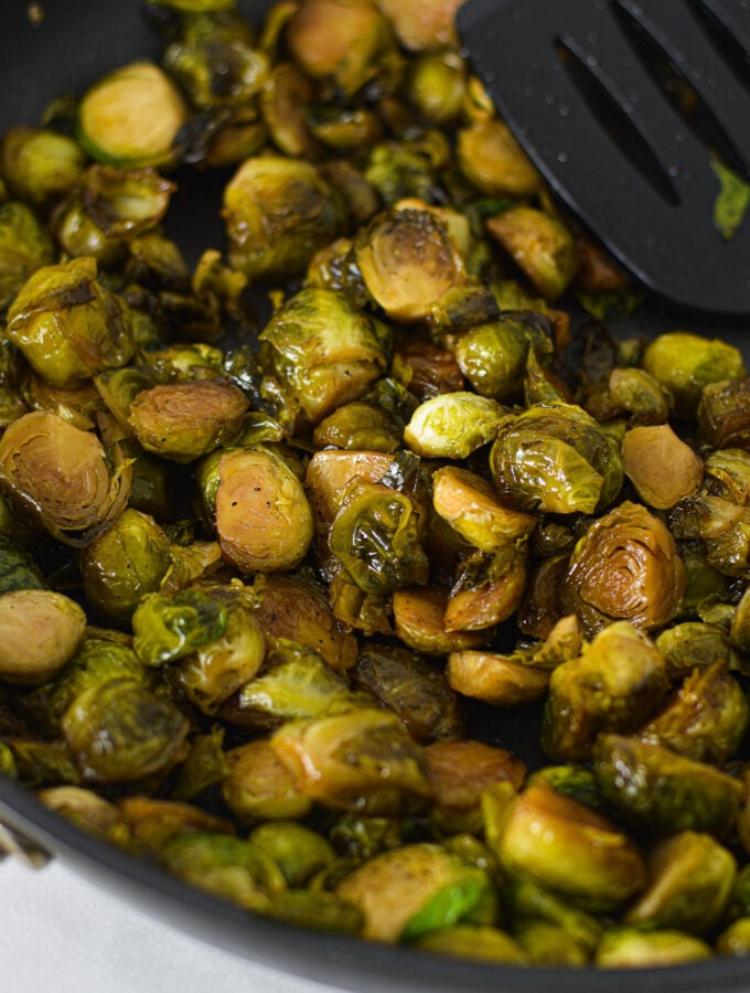 Some lightly browned Stovetop Balsamic Honey Brussels Sprouts in a large skillet, with a large spatula resting on top of the cooked brussels sprouts.