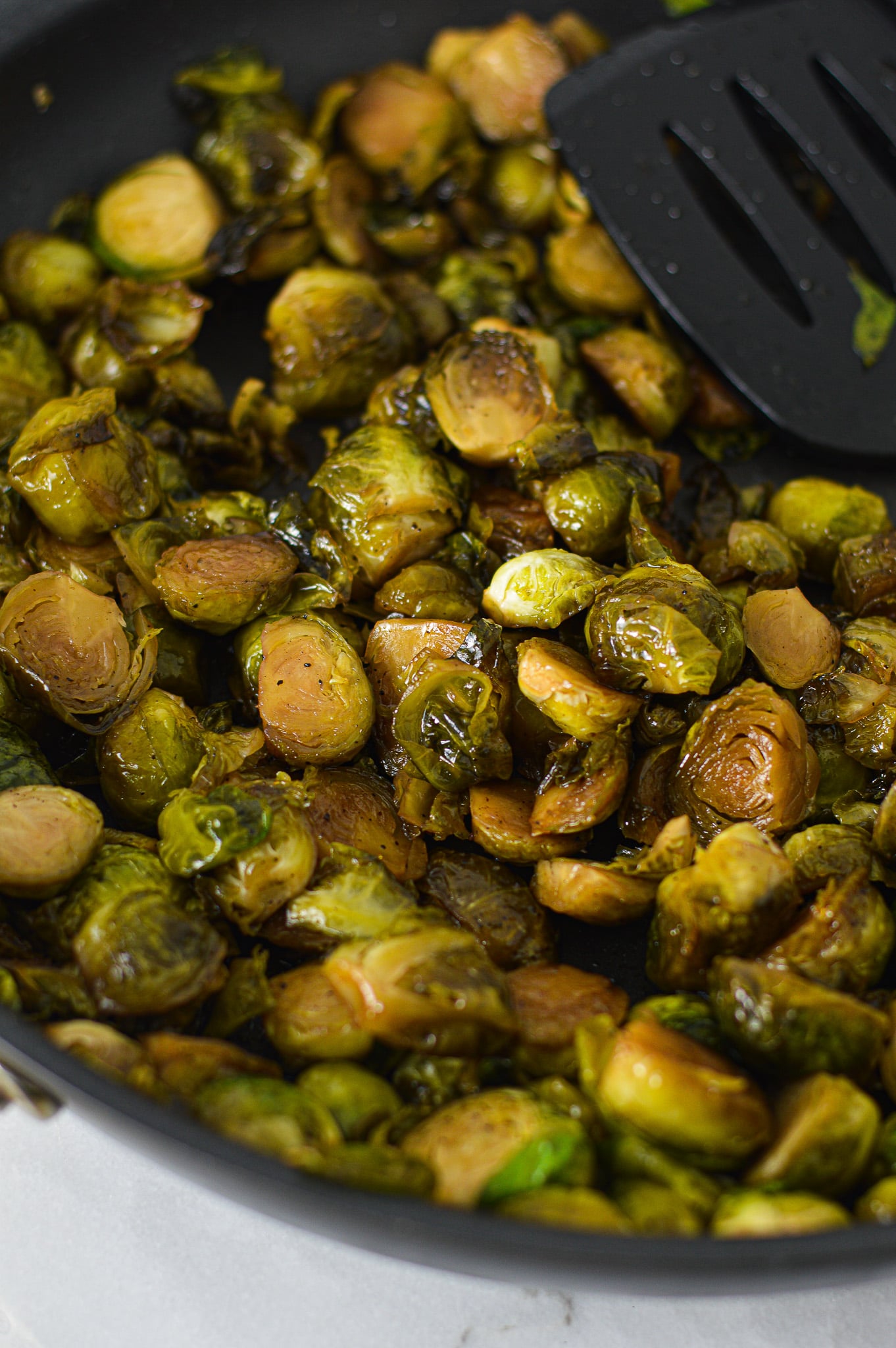 Some lightly browned Stovetop Balsamic Honey Brussels Sprouts in a large skillet, with a large spatula resting on top of the cooked brussels sprouts.