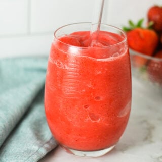 A glass of Virgin Frozen Strawberry Daiquiri on a granite surface, with fresh strawberries in the background giving the drink a refreshingly fresh feel.