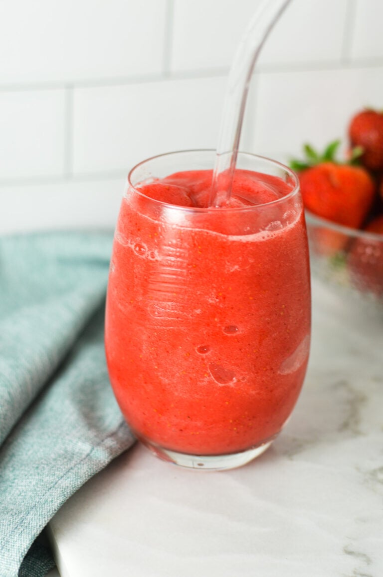 A glass of Virgin Frozen Strawberry Daiquiri on a granite surface, with fresh strawberries in the background giving the drink a refreshingly fresh feel.