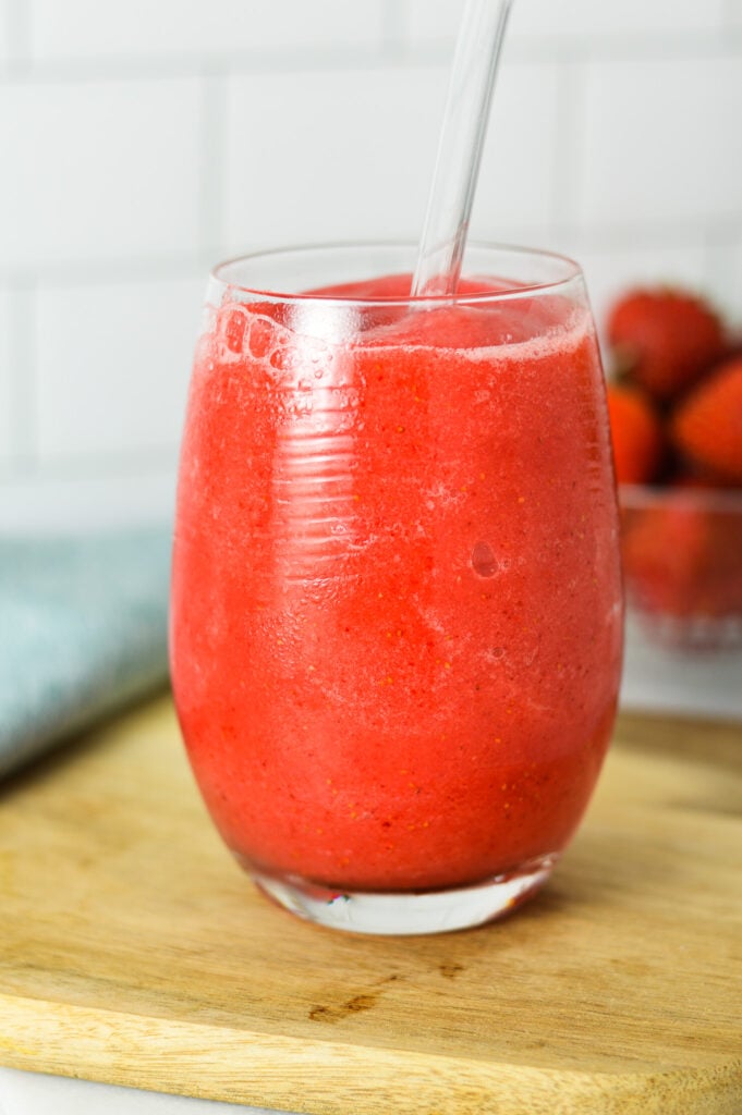 A glass of Virgin Frozen Strawberry Daiquiri, with a plastic straw sticking out of the cold drink. showing how thick and creamy the frozen daiquiri is.