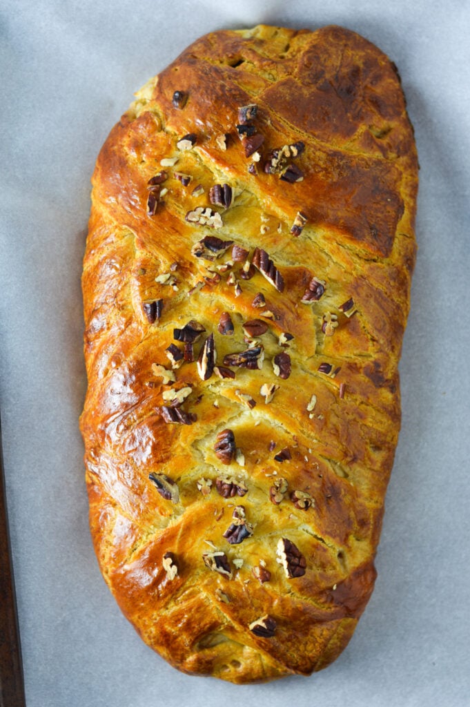 Easy Apple Pecan Cream Cheese Pastry Braid on a parchment paper lined cookie sheet, with the chopped pecans sprinkled over the golden brown bread.