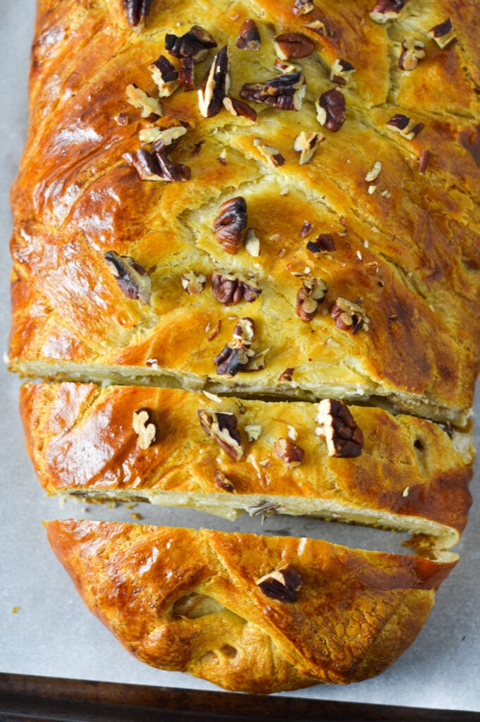 A parchment paper lined cookie tray topped with Easy Apple Pecan Cream Cheese Pastry Braid, with coarsely chopped pecans on top of the golden brown braid.