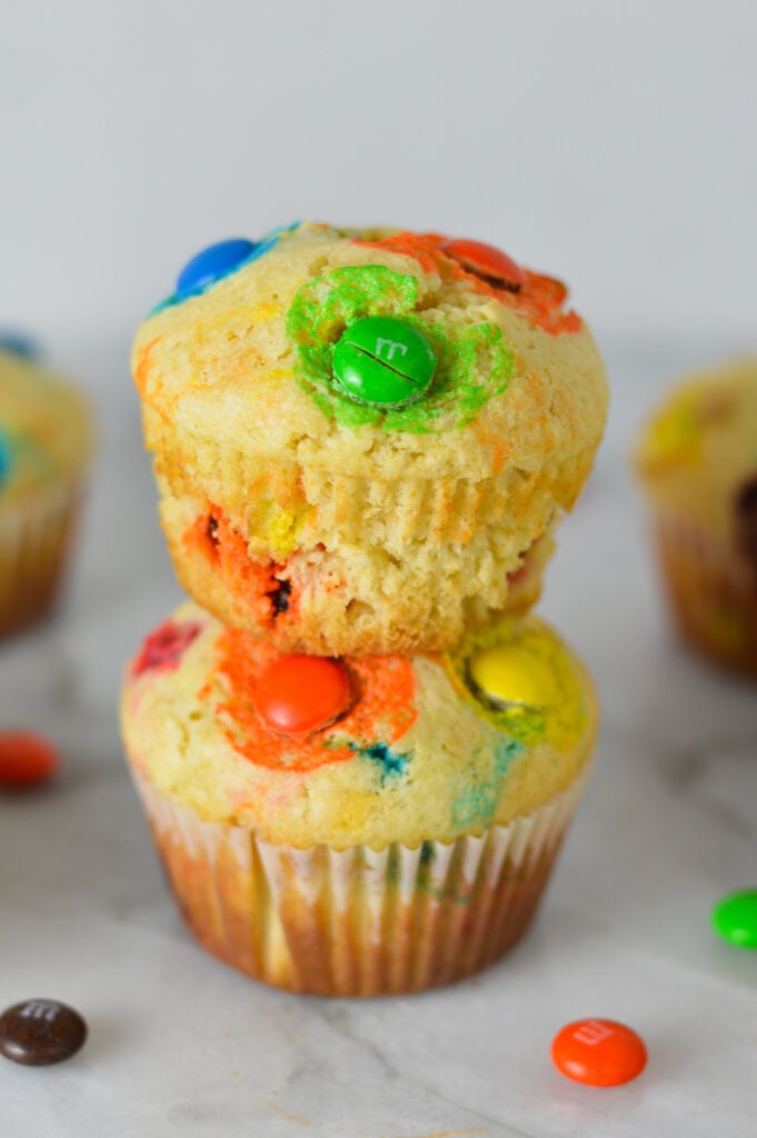 A stack of M&M Muffins with the muffin liners taken off of the top muffin, showing its golden brown color.