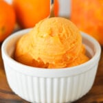 A small bowl full of Ninja Creami Cara Cara Orange Sorbet with a small spoon sticking out of the cold treat.
