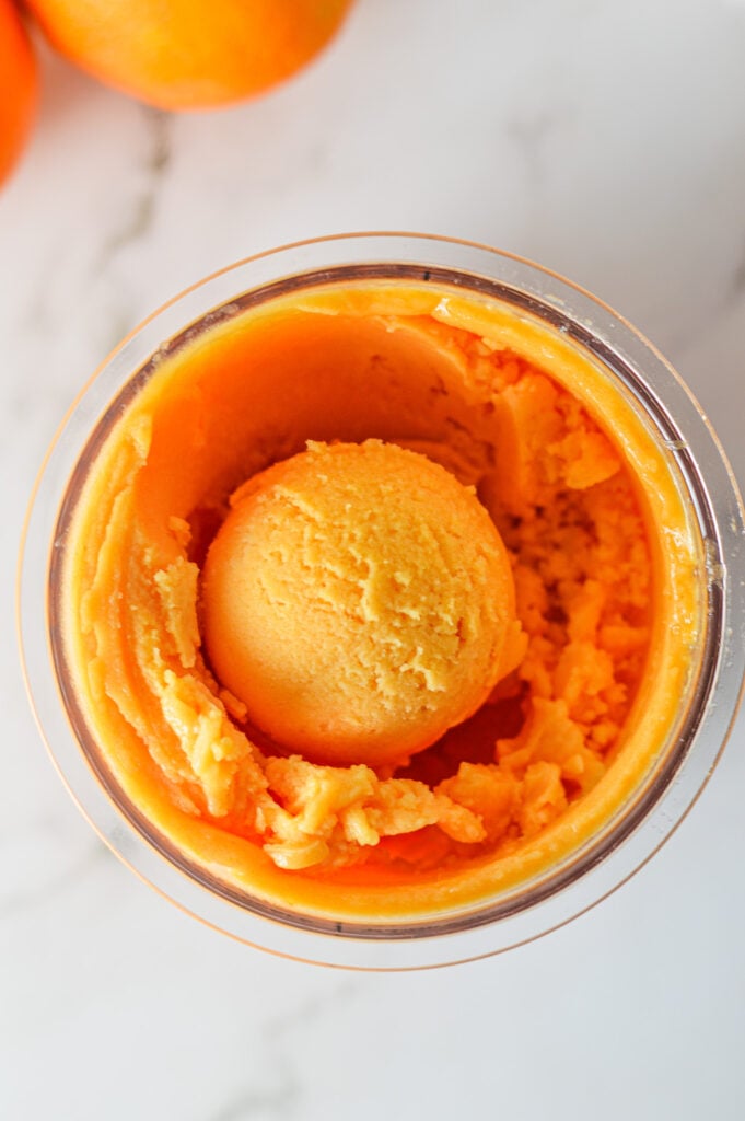 A Ninja Creami container filled with Ninja Creami Cara Cara Orange Sorbet, with a scoop on top showing its smooth texture.