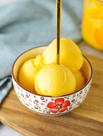 A small bowl full of Ninja Creami Peach Sorbet, with a small spoon inside the scoops of sorbet.