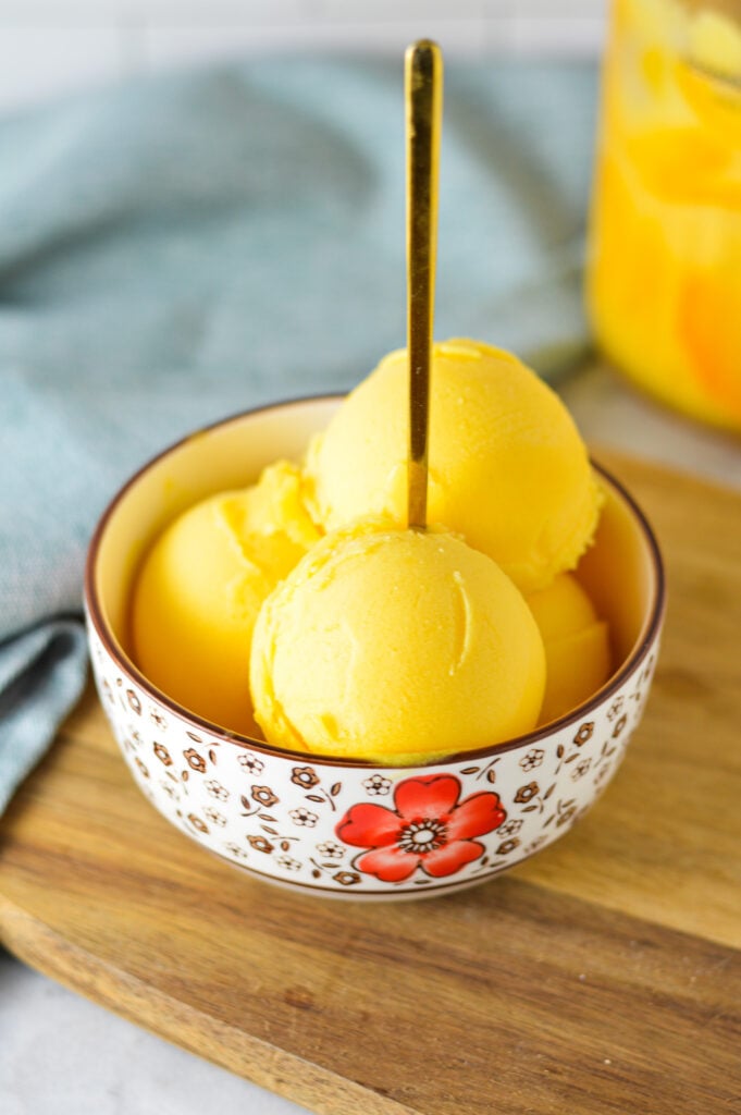 A small bowl full of Ninja Creami Peach Sorbet, with a small spoon inside the scoops of sorbet.