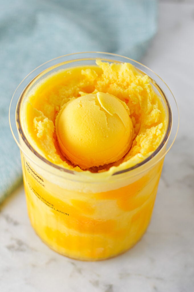 A Ninja Creami container filled with Ninja Creami Peach Sorbet, with a scoop on top of the creamy sorbet.