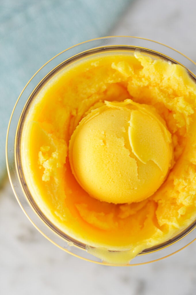 A Ninja Creami pint container filled with Ninja Creami Peach Sorbet, with a scoop on top showing the smooth texture.