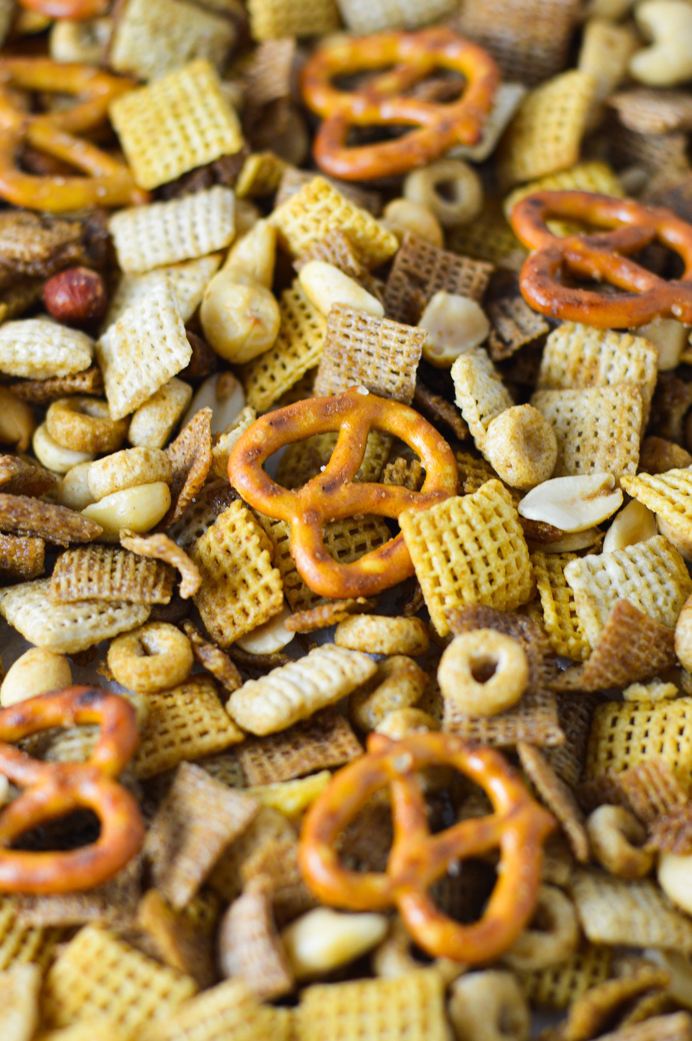 A parchment paper lined baking sheet filled with freshly baked Bold Chex Mix, with the crunchy nut and Chex cereal mix golden brown.