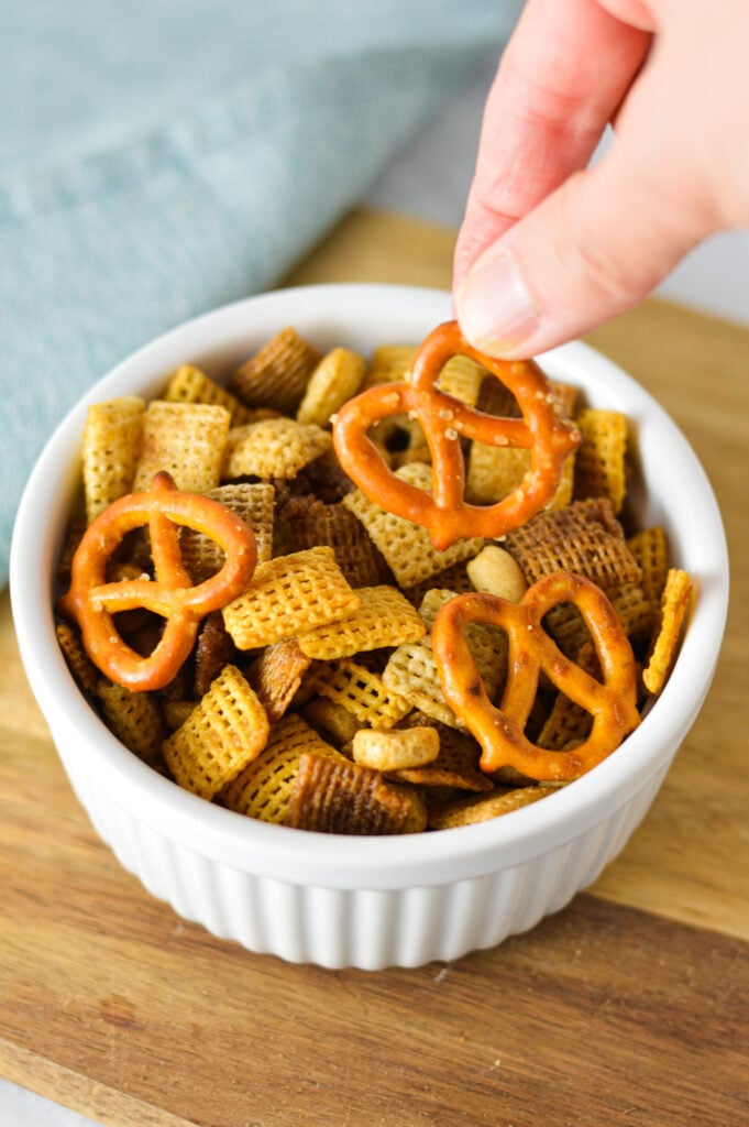 A hand taking some Bold Chex Mix out of a small bowl, showing the crunchy snack mixture.