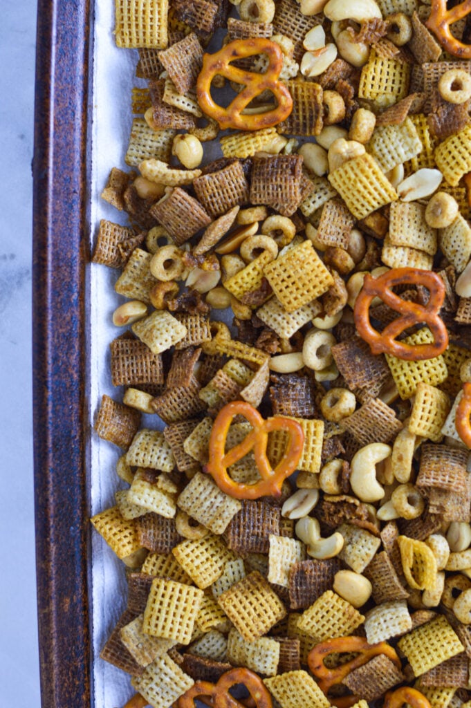 A cookie sheet lined with parchment paper filled with homemade Chex Mix, with the mini pretzel twists golden brown against the mixture of rice, rice and wheat chex cereal.