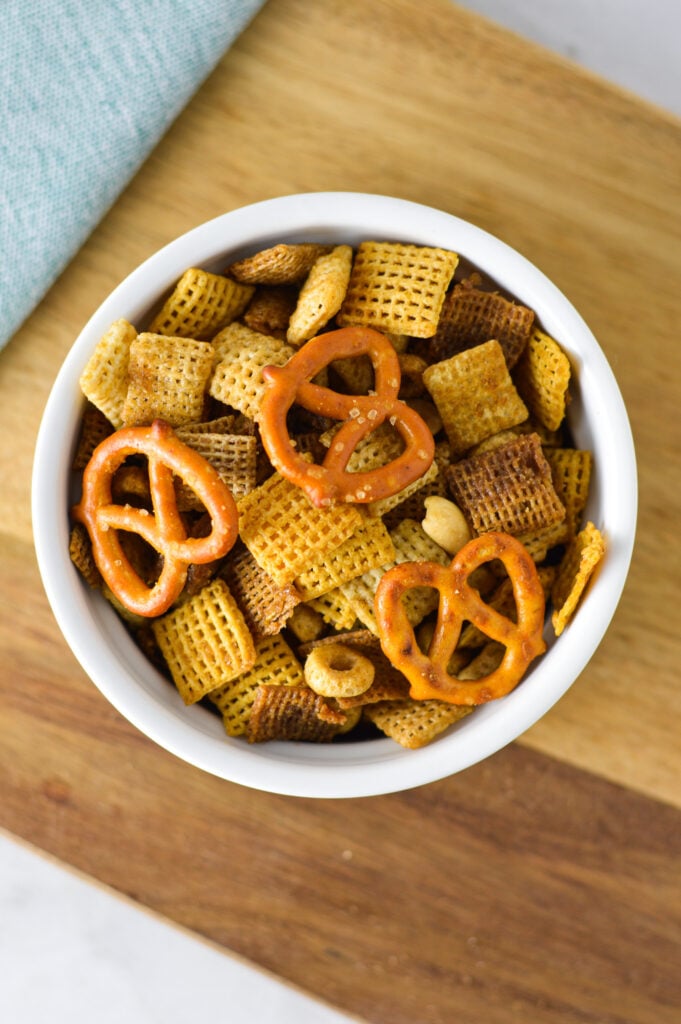 A small white bowl filled with Bold Chex Mix on a wooden surface.