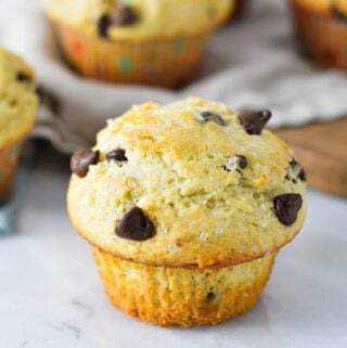 Some fluffy Chocolate Chip Muffins on a granite surface, with the paper liners taken off of the front muffin.