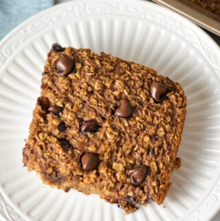 A square slice of Double Chocolate Baked Oatmeal on a small plate, with some freshly baked chocolate oatmeal in the 9x9 pan.