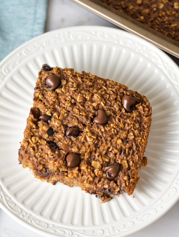 A square slice of Double Chocolate Baked Oatmeal on a small plate, with some freshly baked chocolate oatmeal in the 9x9 pan.