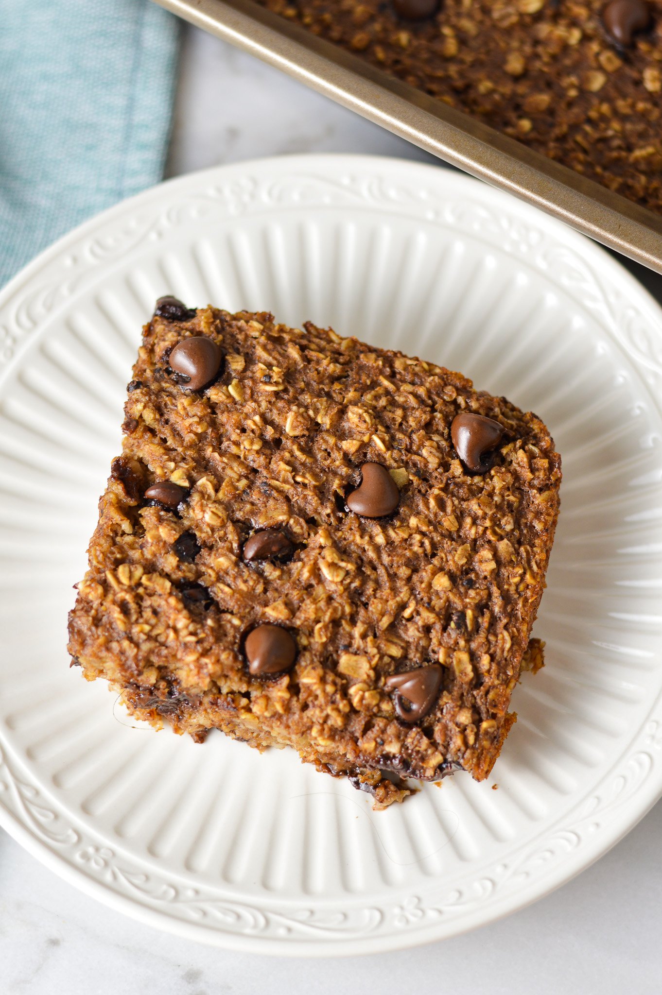 A square slice of Double Chocolate Baked Oatmeal on a small plate, with some freshly baked chocolate oatmeal in the 9x9 pan.
