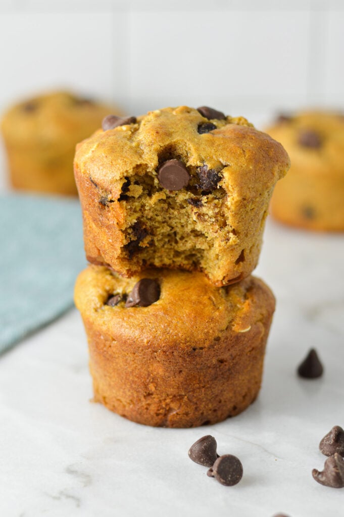 A stack of Healthy Peanut Butter Chocolate Chip Oat Muffins with a bite taken out of the top muffin, showing the fluffy texture.