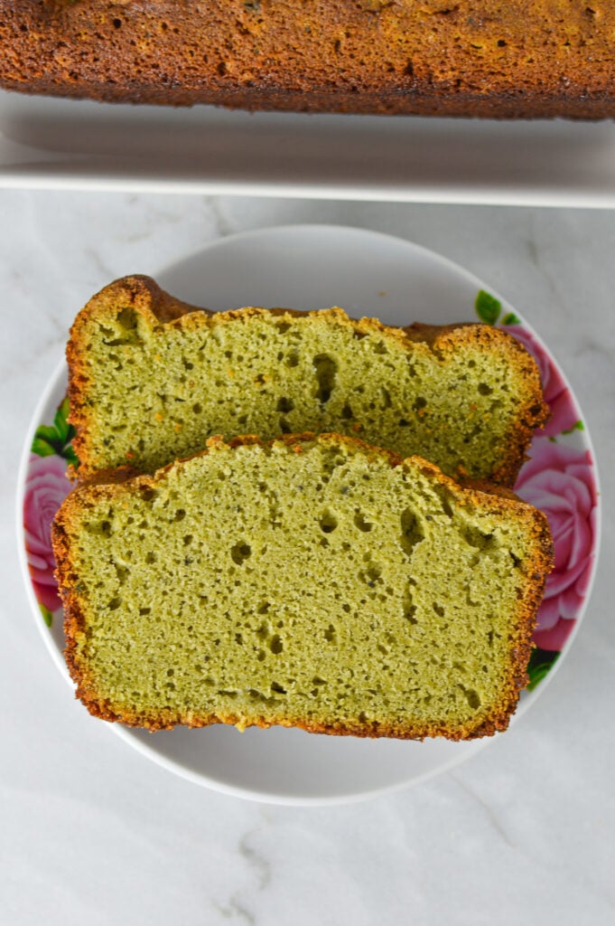 A couple of slices of Matcha Pound Cake on a small plate, with the cut matcha loaf in the background.