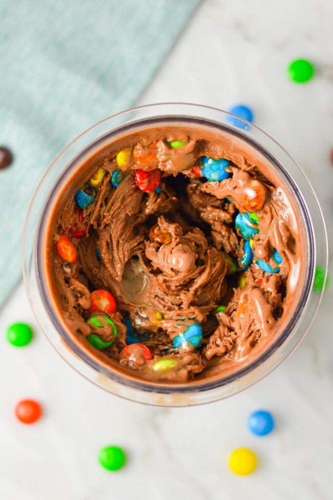 A Ninja Creami container filled with freshly made Ninja Creami 3 Ingredient M&M Chocolate Ice Cream on a granite surface.
