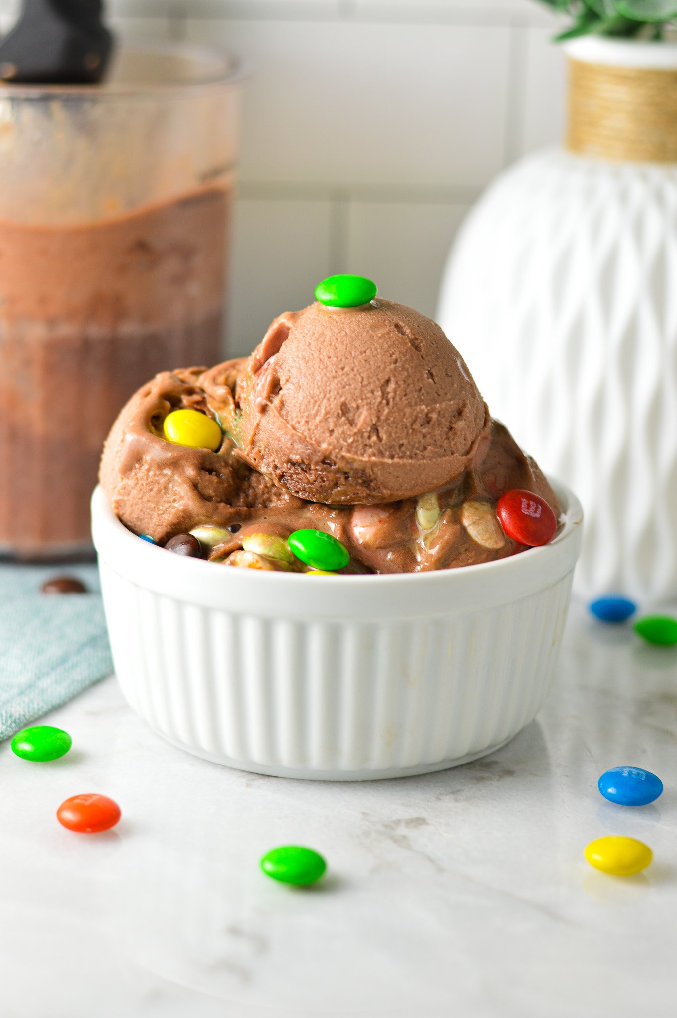 A small white bowl filled with Ninja Creami 3 Ingredient M&M Chocolate Ice Cream, with some chocolate M&Ms surrounding the Ninja Creami chocolate ice cream.