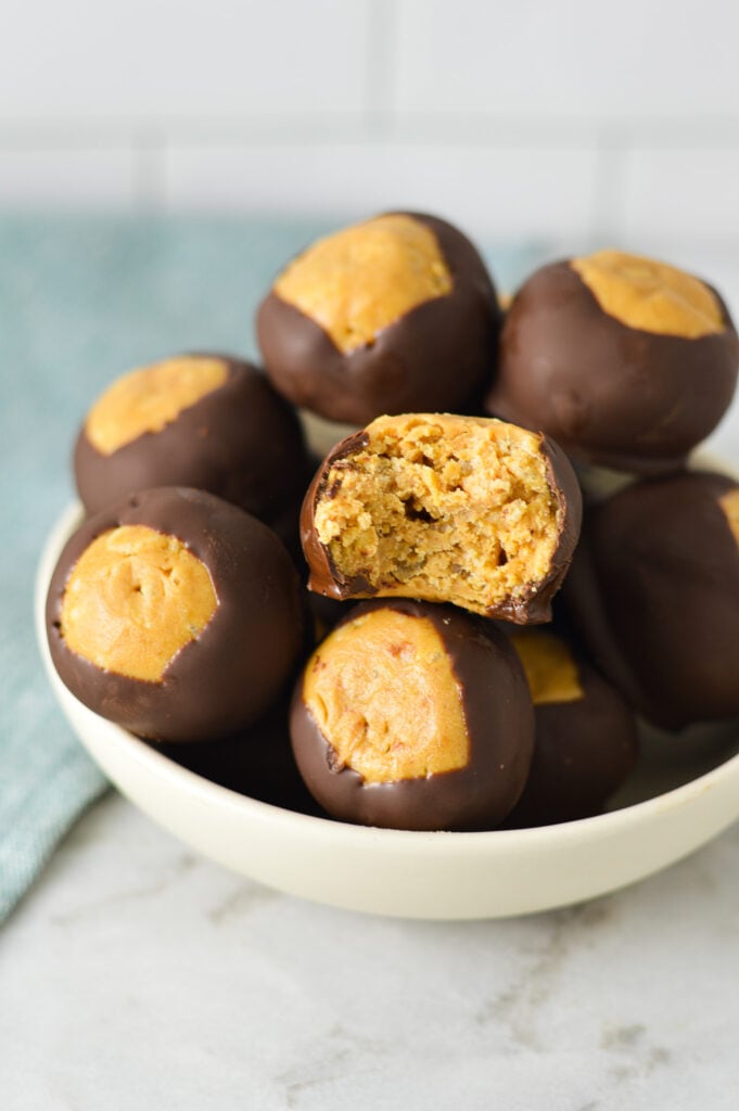 A small bowl full of Rice Krispie Buckeyes, with a bite taken out of one of them showing the crispy texture.