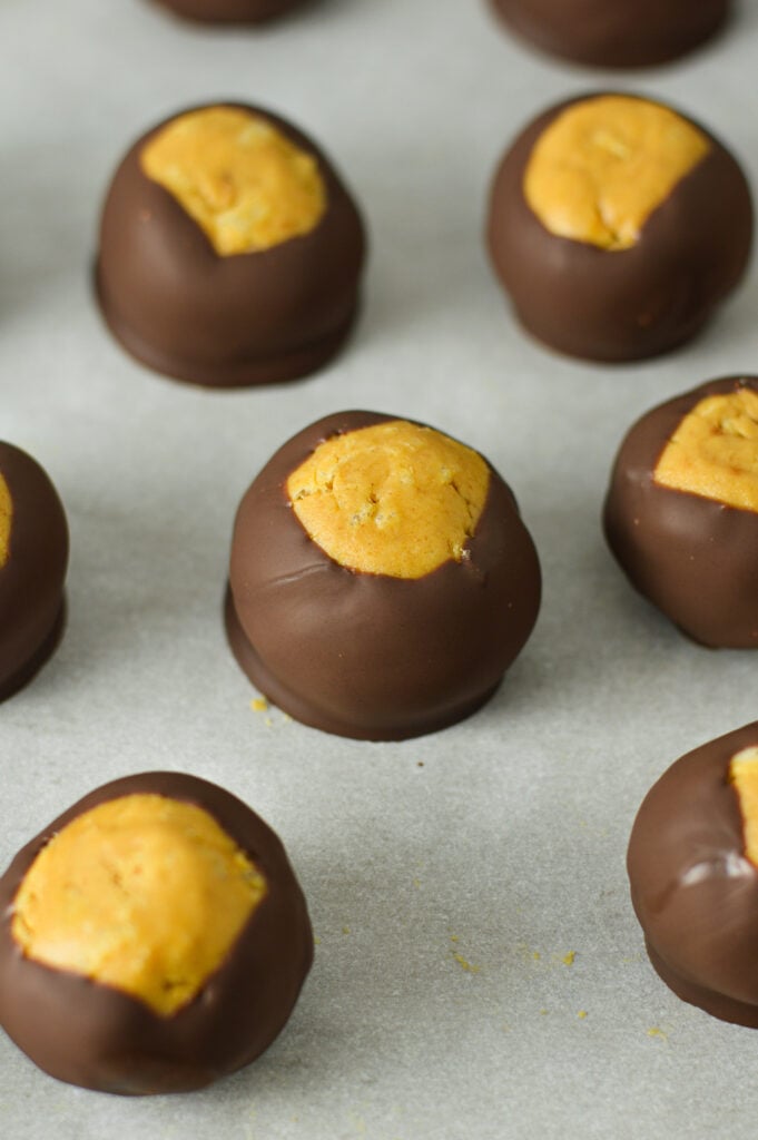 A parchment paper lined baking sheet topped with Rice Krispie Buckeyes.