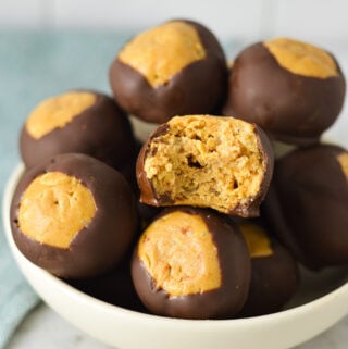 A small bowl filled with Rice Krispie Buckeyes, with a bite taken out of one of the Buckeye balls, showing the extra texture the Rice Krispies cereal gives.