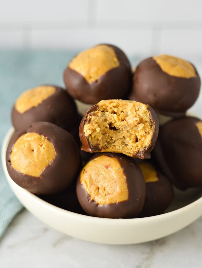 A small bowl filled with Rice Krispie Buckeyes, with a bite taken out of one of the Buckeye balls, showing the extra texture the Rice Krispies cereal gives.