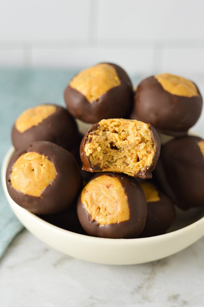 A small bowl filled with Rice Krispie Buckeyes, with a bite taken out of one of the Buckeye balls, showing the extra texture the Rice Krispies cereal gives.