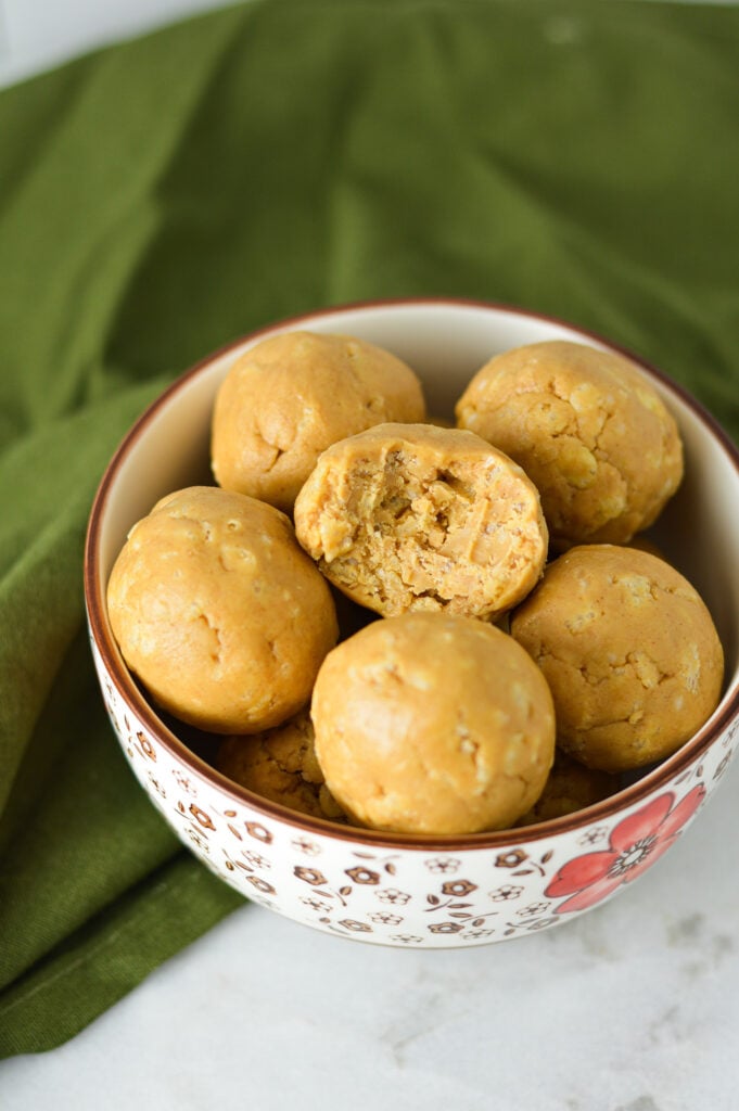 A small bowl filled with Rice Krispies Peanut Butter Balls, with a bite taken out of one of the peanut butter balls showing the crunchy texture.