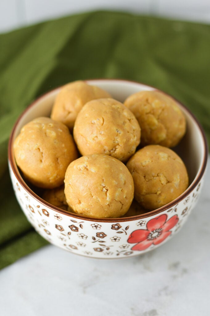 A small bowl with Rice Krispies Peanut Butter Balls, with the Rice Krispie cereal showing through the no bake peanut butter balls.
