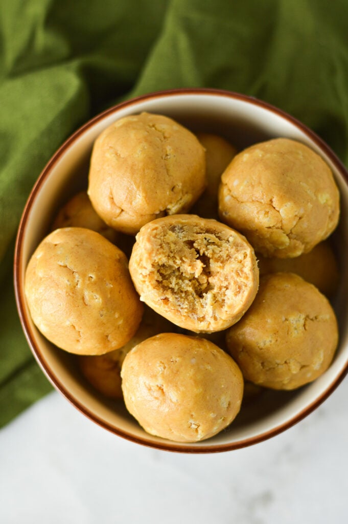 Some Rice Krispies Peanut Butter Balls in a small bowl, with a bite taken out of one of the no bake balls, showing the crispy rice cereal in the peanut butter ball.