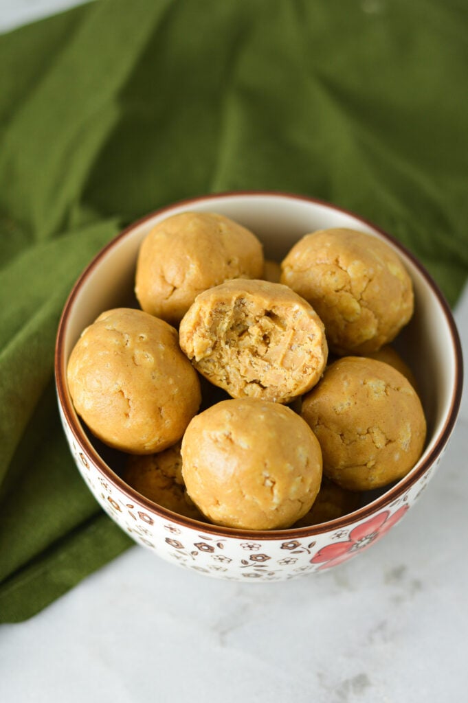 A small bowl filled with Rice Krispies Peanut Butter Balls, with a bite taken out of one of the balls showing the crispy texture.