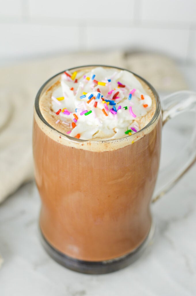 A tall glass full of Cake Batter Mocha, topped with whipped cream and rainbow sprinkles.