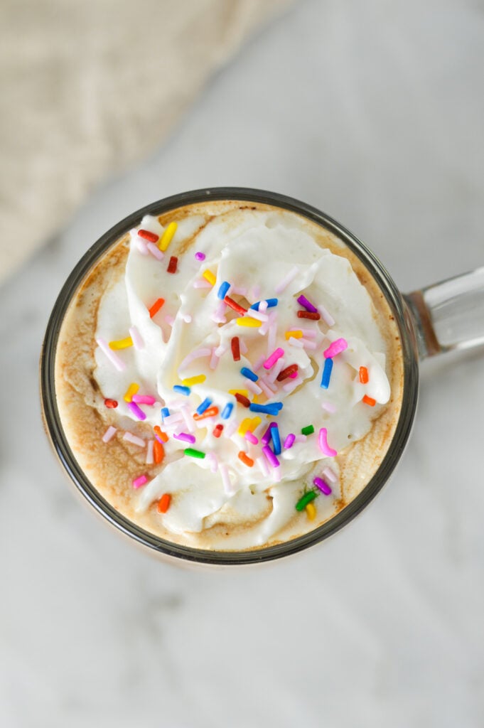 An overhead shot of a cup of Cake Batter Mocha, topped with whipped cream and rainbow candy sprinkles.