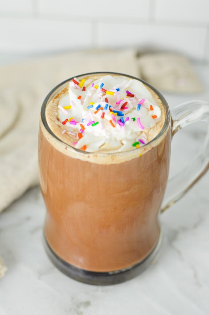 A large glass mug filled with Cake Batter Mocha, topped with sweet whipped cream and festive sprinkles.