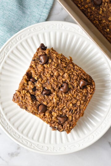 A square slice of Double Chocolate Baked Oatmeal on a small plate, with some freshly baked chocolate oatmeal in the 9x9 pan.