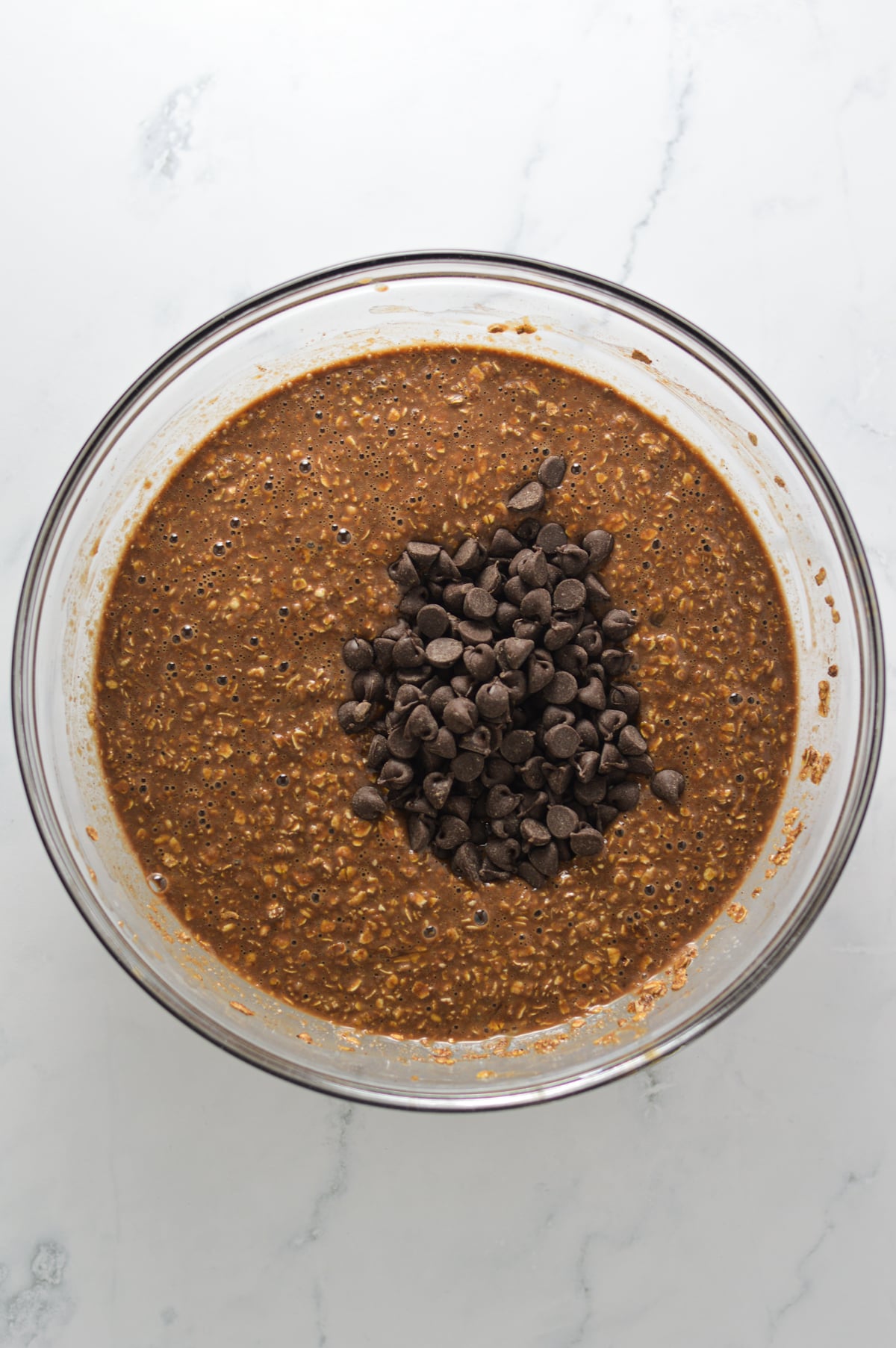 Double Chocolate Baked Oatmeal batter in a large glass bowl, with the semi-sweet chocolate chips resting on top.