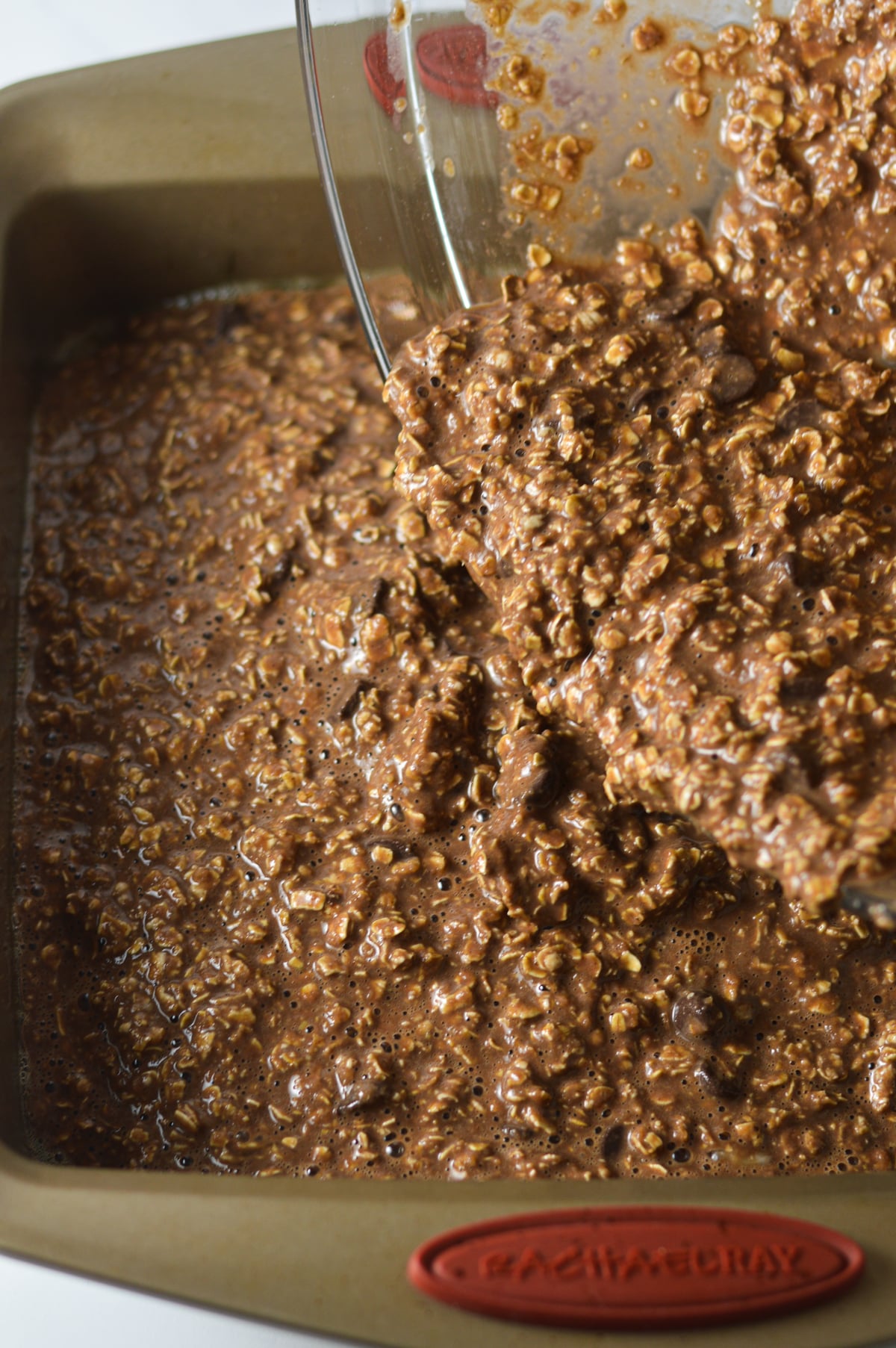 The chocolate oatmeal mixture being poured into a square pan.