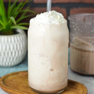 A glass filled with Ninja Creami Frozen Hot Chocolate, topped with whipped cream and a clear plastic straw sticking out of the thick drink.