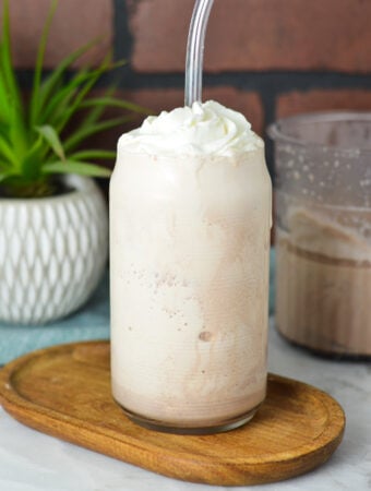 A glass filled with Ninja Creami Frozen Hot Chocolate, topped with whipped cream and a clear plastic straw sticking out of the thick drink.