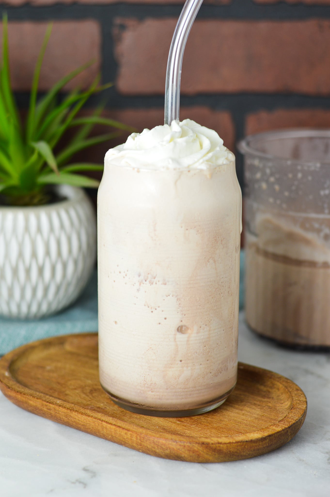 A glass filled with Ninja Creami Frozen Hot Chocolate, topped with whipped cream and a clear plastic straw sticking out of the thick drink.