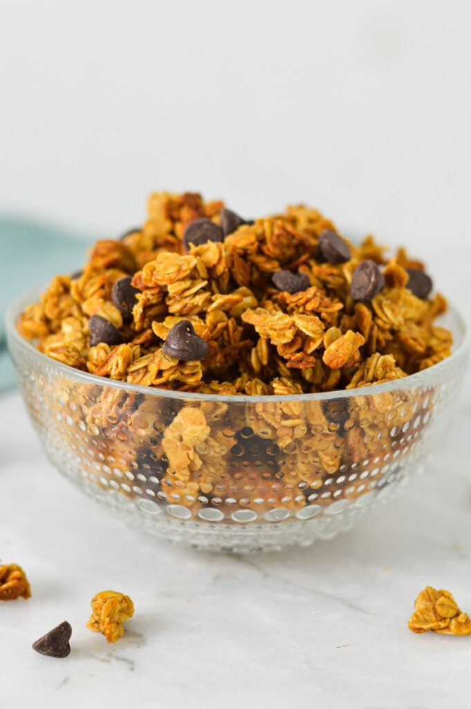 A small mixing bowl filled with Peanut Butter Chocolate Chip Granola, with the peanut butter granola clusters golden brown against the extra chocolate chips on top.