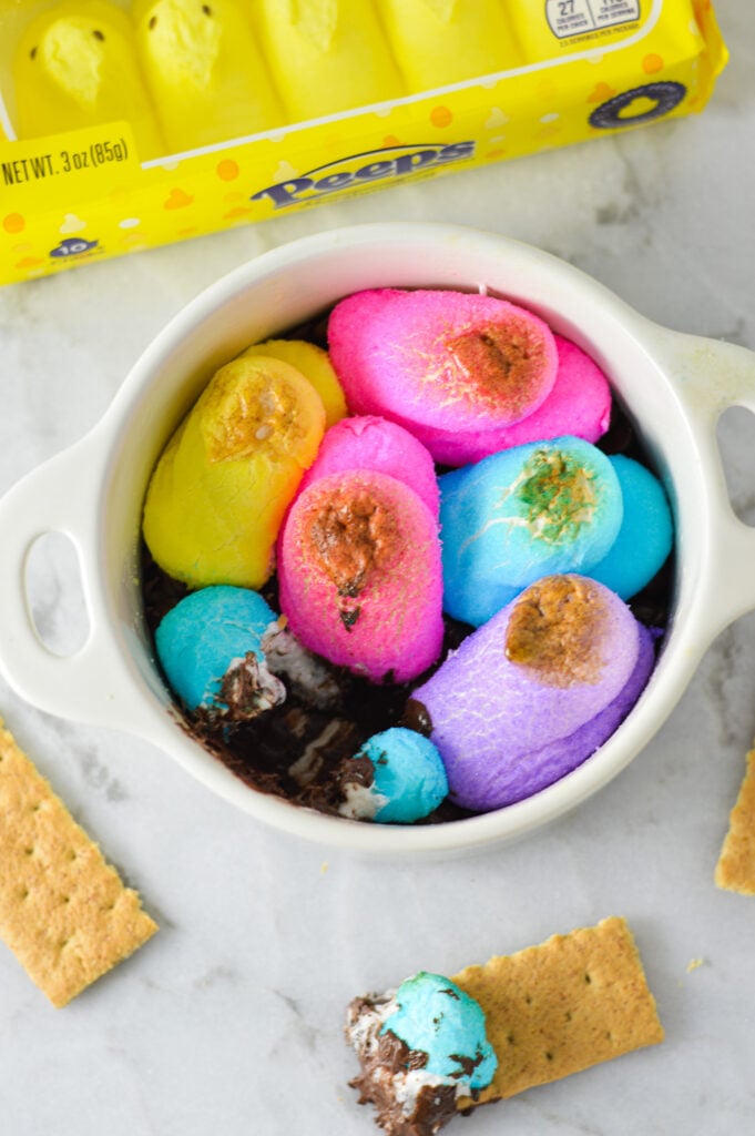 A small white container filled with Peeps S'mores Dip, with the colorful Peeps marshmallows a little golden brown.