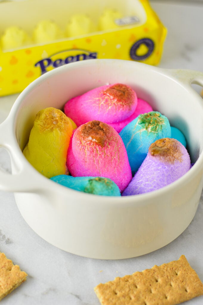 A large ramekin filled with colorful Peeps S'mores Dip, with the Peep chicks slightly golden brown from being broiled in the oven.